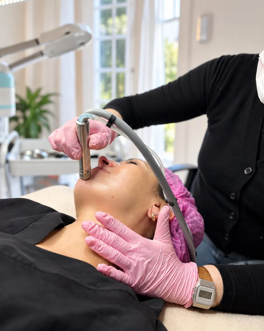 Una profesional del centro aplicando un tratamiento facial a una clienta acostada en la camilla.